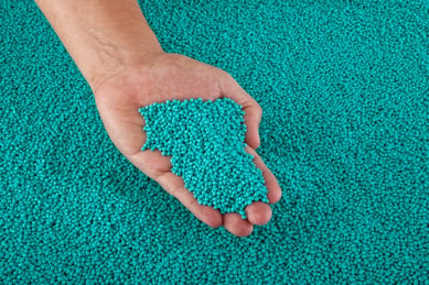 teal resin color additive pellets in a person's hand
